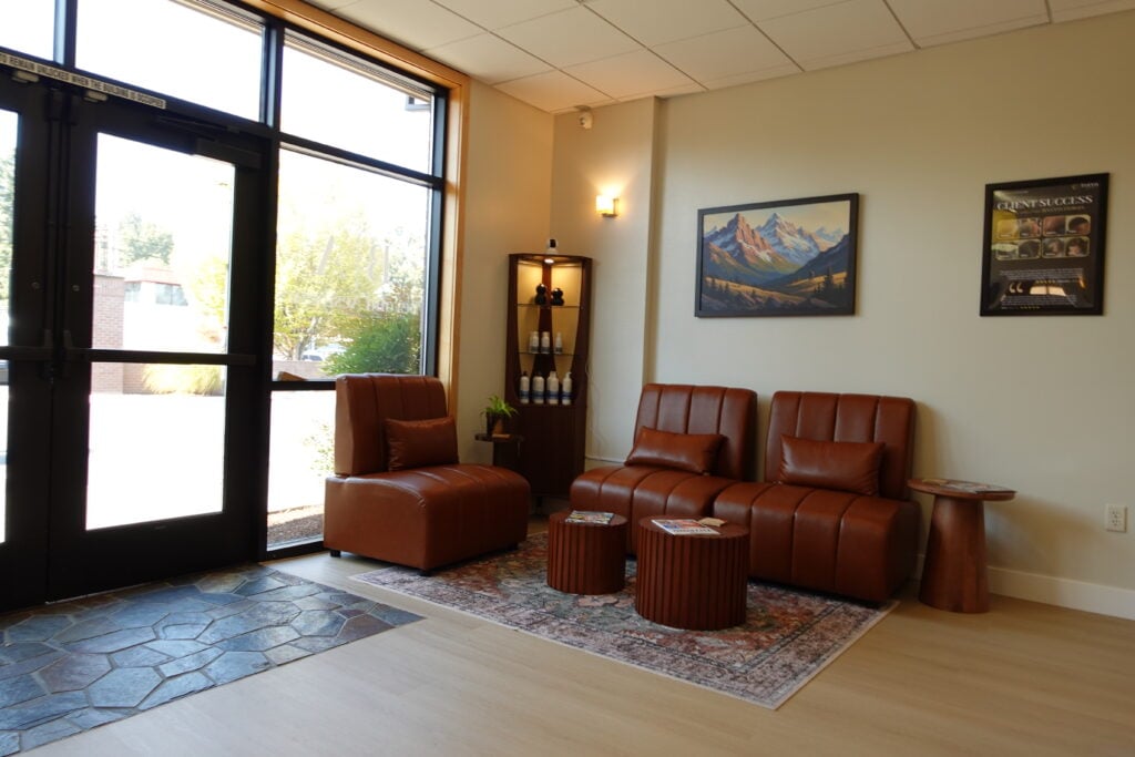 Comfortable waiting room lobby with brown leather seating, product display shelves, and large glass entry doors.